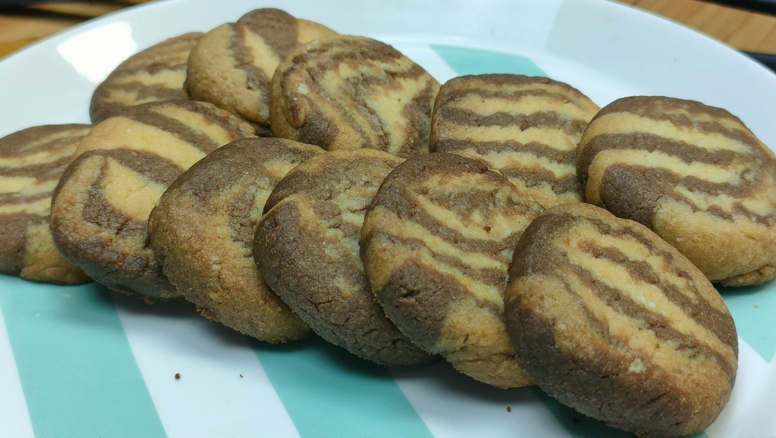 Foto dei biscotti bicolore fatti in casa, preparati con una frolla a due colori (vaniglia e cacao), disposti elegantemente su una teglia rivestita di carta forno. L'immagine evidenzia la texture morbida e la superficie leggermente dorata dei biscotti.