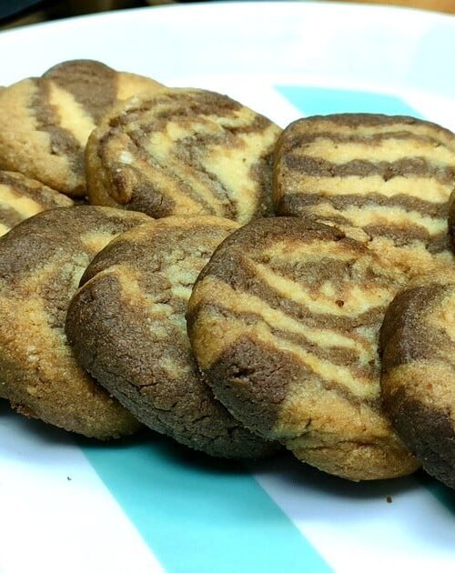 Foto dei biscotti bicolore fatti in casa, preparati con una frolla a due colori (vaniglia e cacao), disposti elegantemente su una teglia rivestita di carta forno. L'immagine evidenzia la texture morbida e la superficie leggermente dorata dei biscotti.