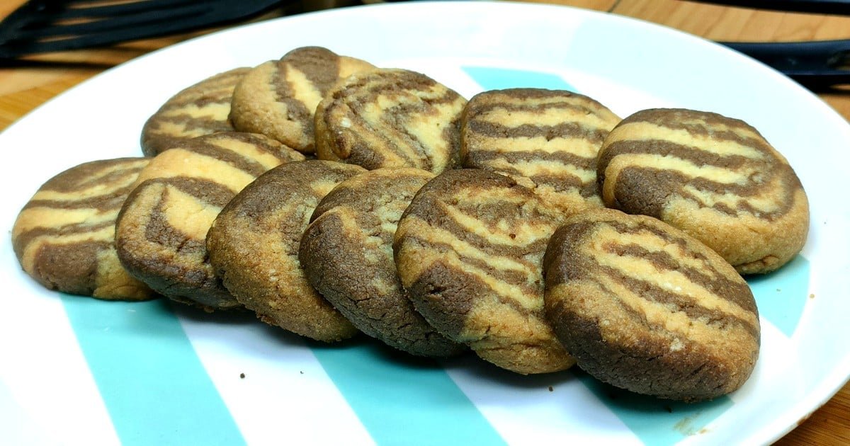 Foto dei biscotti bicolore fatti in casa, preparati con una frolla a due colori (vaniglia e cacao), disposti elegantemente su una teglia rivestita di carta forno. L'immagine evidenzia la texture morbida e la superficie leggermente dorata dei biscotti.